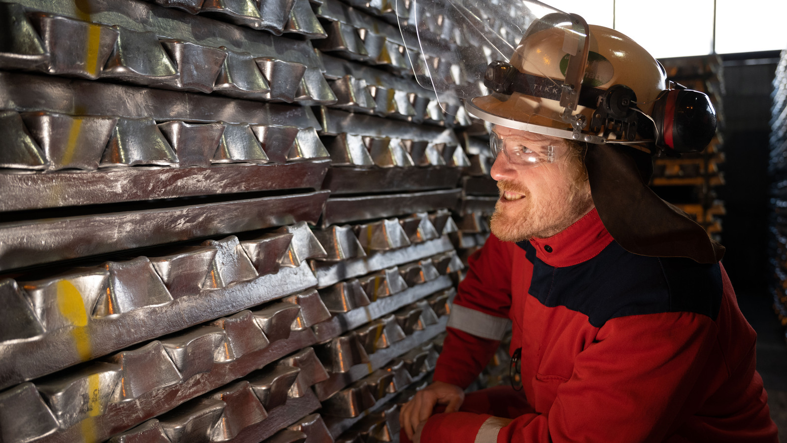 a man wearing a hard hat next to a stack of aluminium billets